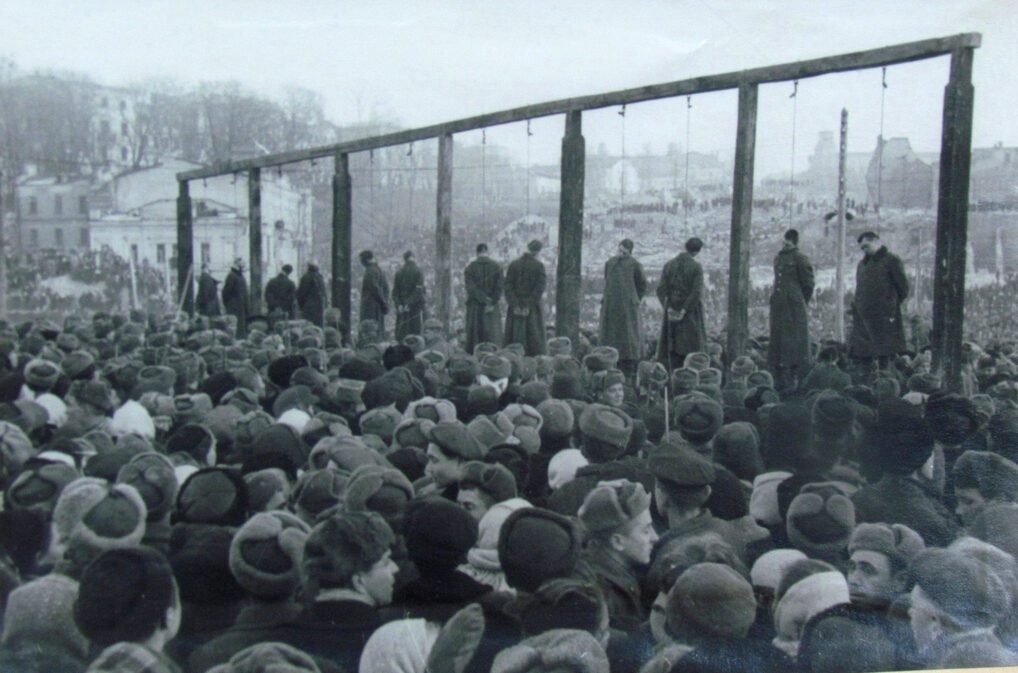 Zdjęcie z egzekucji hitlerowskich zbordniarzy. Na fotografii widzimy drewnianą szubienicę i powieszonych skazańców. Wokół nich zgromadził się tłum ludzi, który przyszli zobaczyć wydarzenie. W tle znalazło się kilka budynków