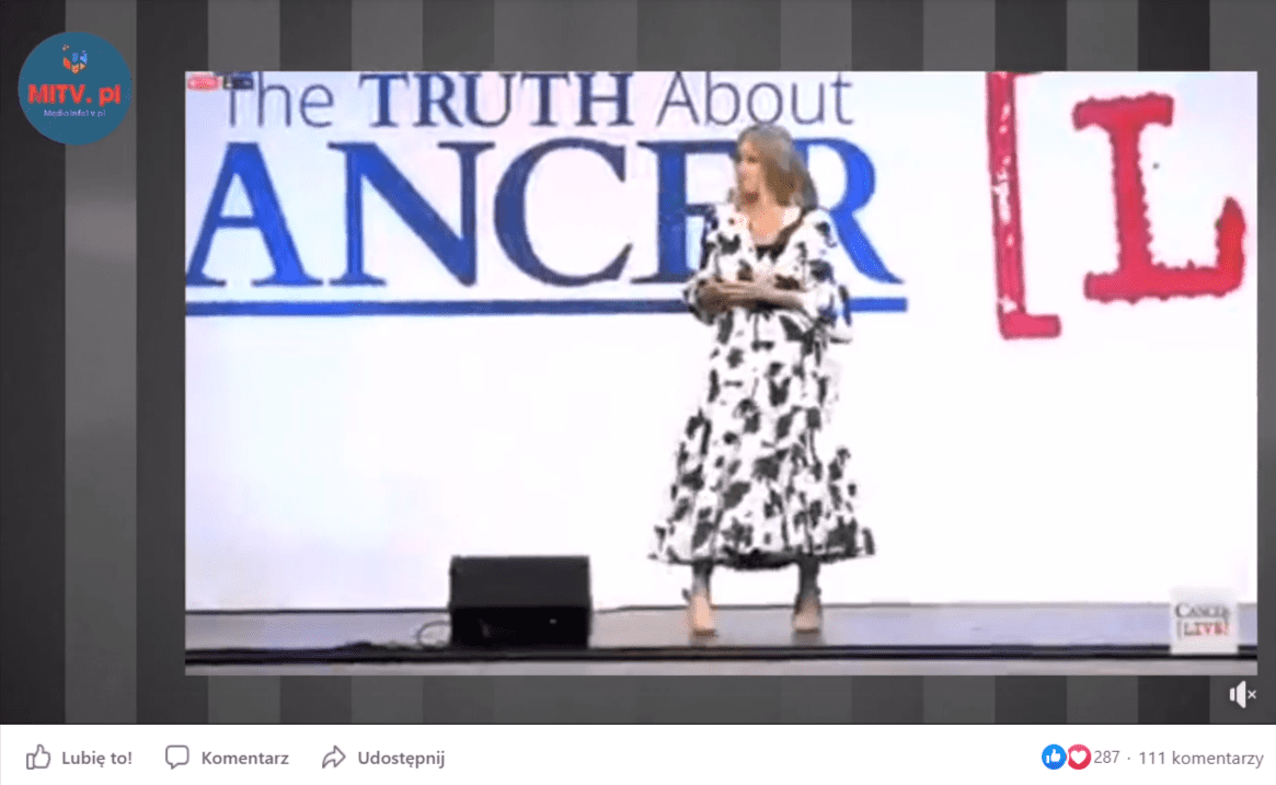 Zrzut ekranu przedstawiający film zamieszczony na Facebooku. Na zatrzymanej klatce nagrania widać, że Carrie Madej stoi ubrana w czarno-białą sukienkę na scenie. W tle znajdują się niebieskie i czerwone napisy, które w całości nie zmieściły się w kadrze.