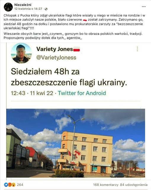 Wpis na Facebooku dotyczący sytuacji, w której mężczyzna ściągający ukraińskie flagi został zatrzymany przez policję. Na zdjęciu widzimy rondo, na którego środku zasadzona została zieleń. Pośrodku ronda stoi latarnia, na które widać zawieszone polskie flagi. W tle znajduje się trzypiętrowy budynek mieszkalny z oknami wychodzącymi na rondo