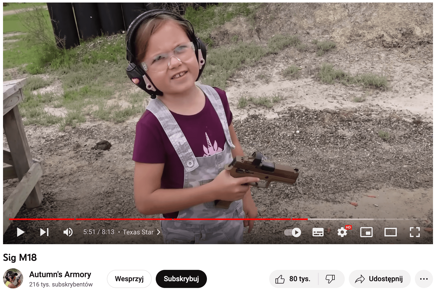 Zrzut ekranu filmu na YouTubie. Widoczna jest kilkuletnia dziewczynka trzymająca w dłoni pistolet.