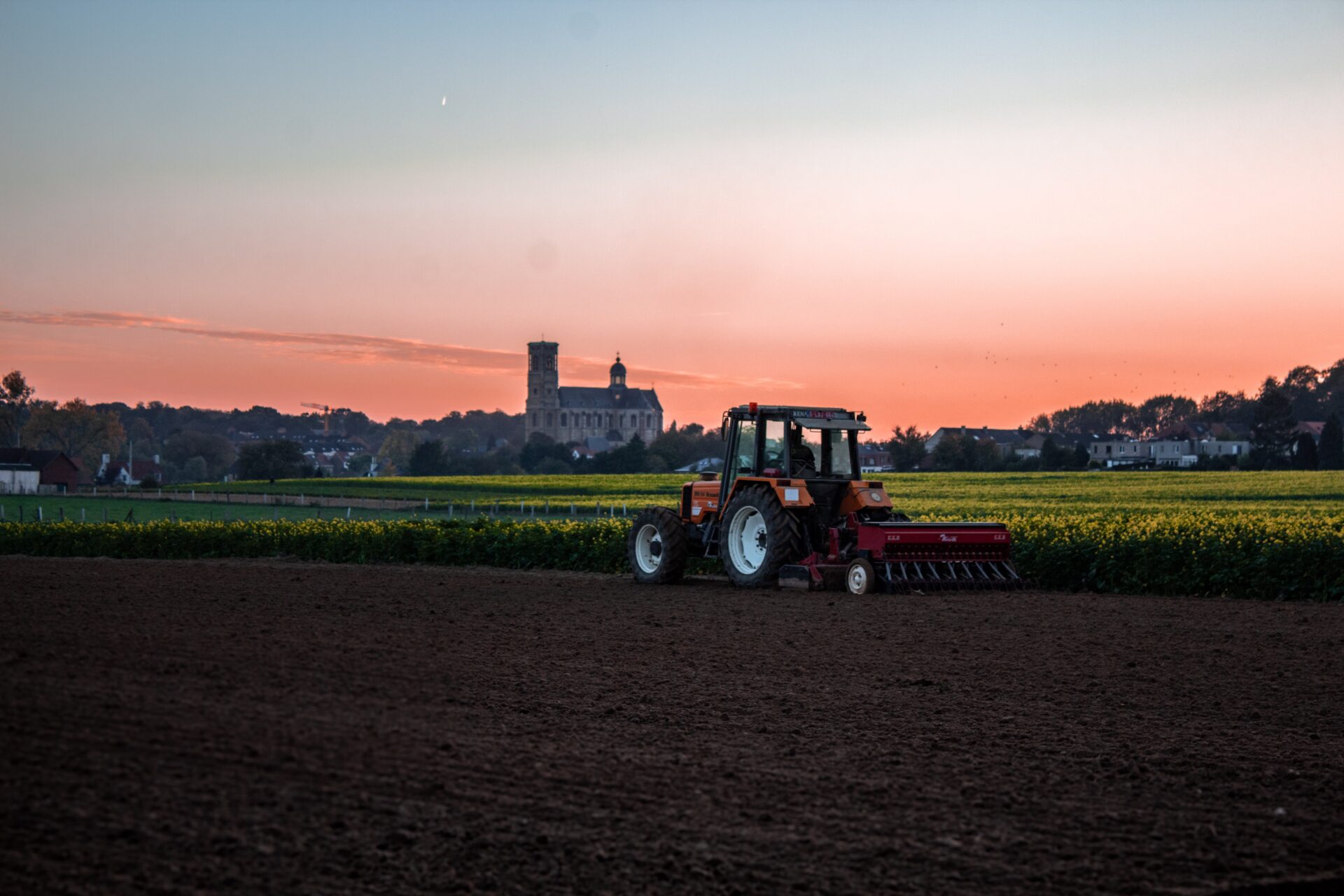 Traktor orzący ziemię pługiem na tle zachodzącego Słońca
