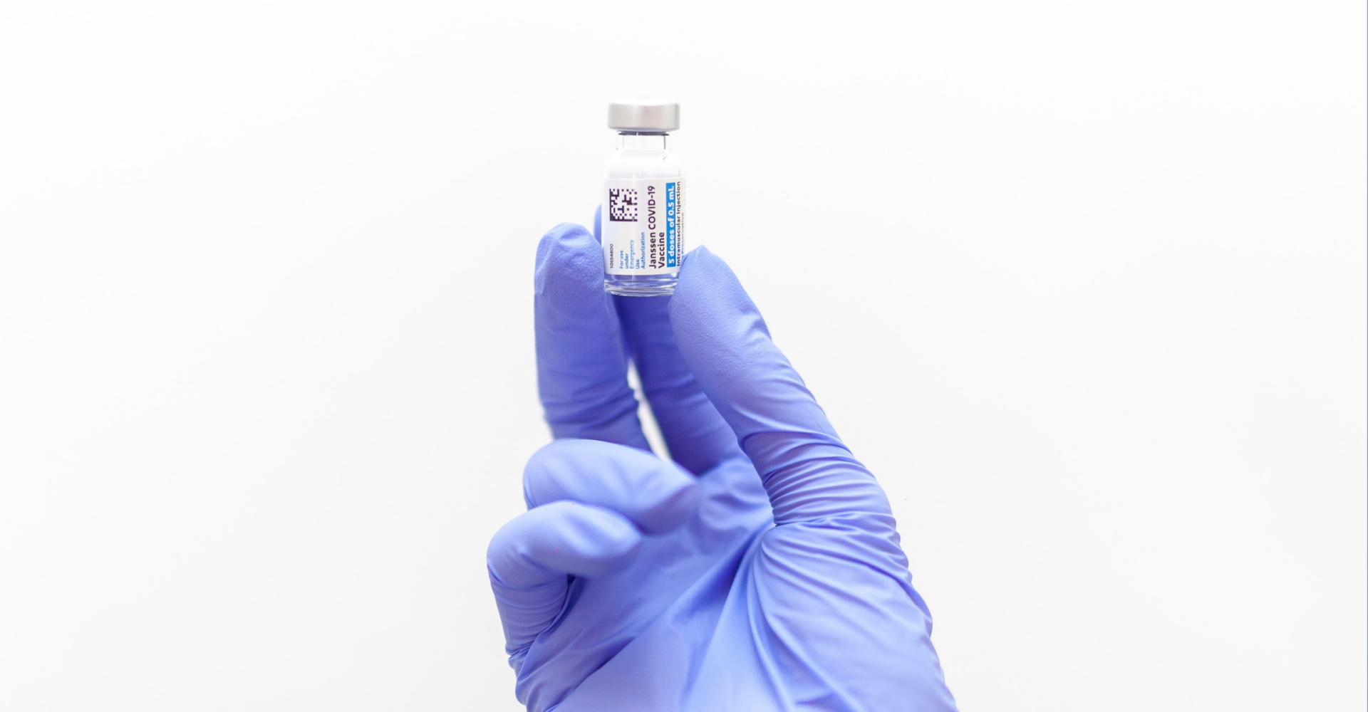 Dłoń w niebieskich rękawiczkach trzyma fiolkę ze szczepionką