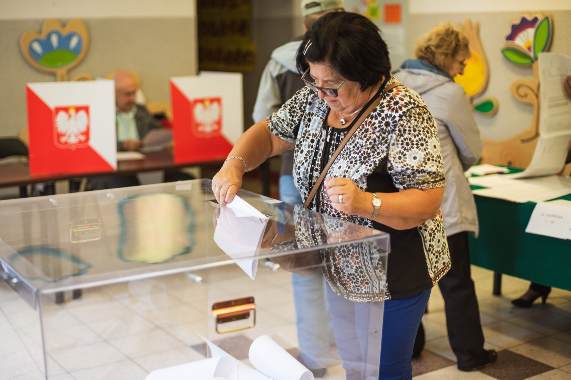 Kobieta w krótkich czarnych włosach wrzuca kartę do głosowania do urny wyborczej.