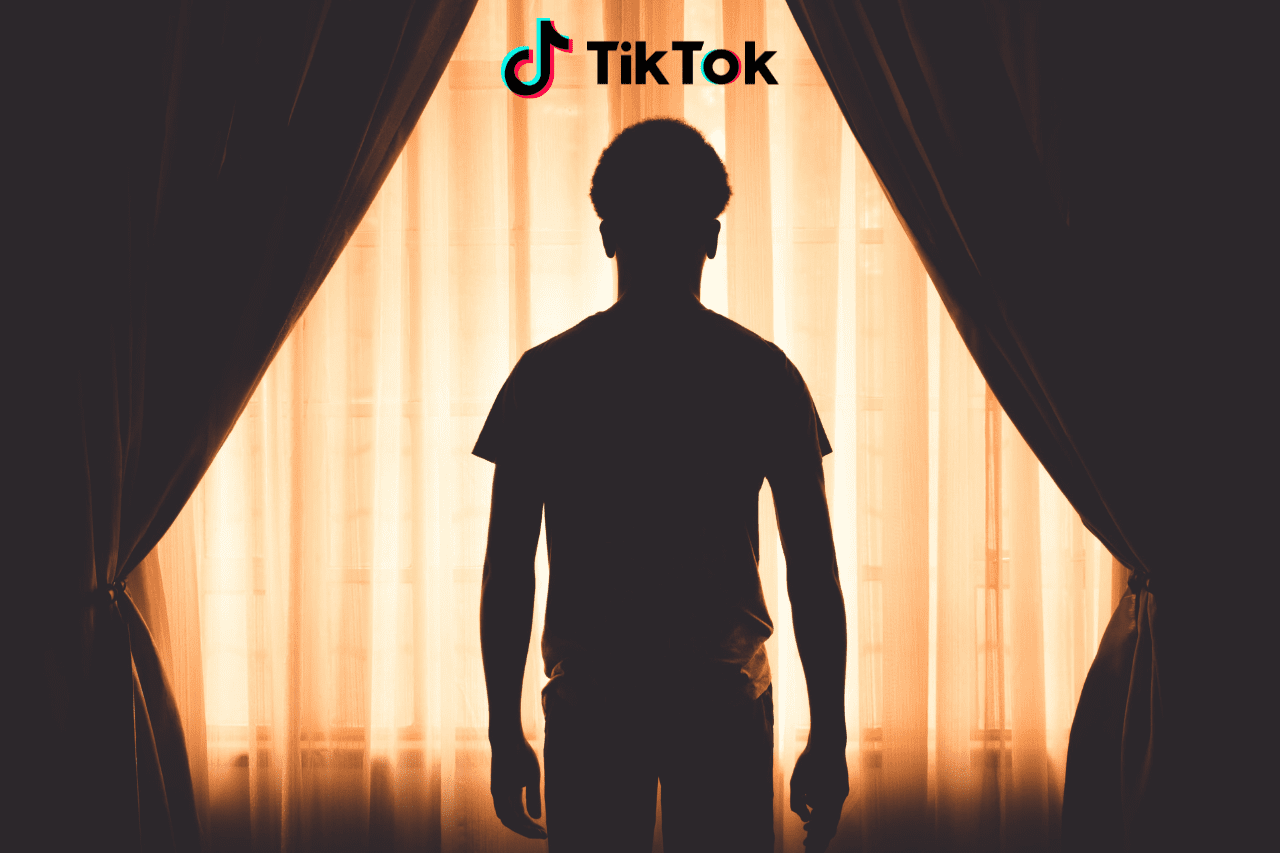 Zacieniona postać stojąca przez zasłoniętym oknem. Nad nią logotyp TikToka.