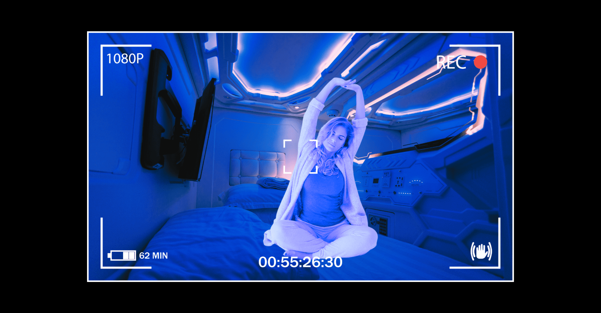 Kobieta ubrana w piżamę wyciąga ręce w górę. Znajduje się w pomieszczeniu pełnym niebieskich świateł LED, siedzi na łóżku.