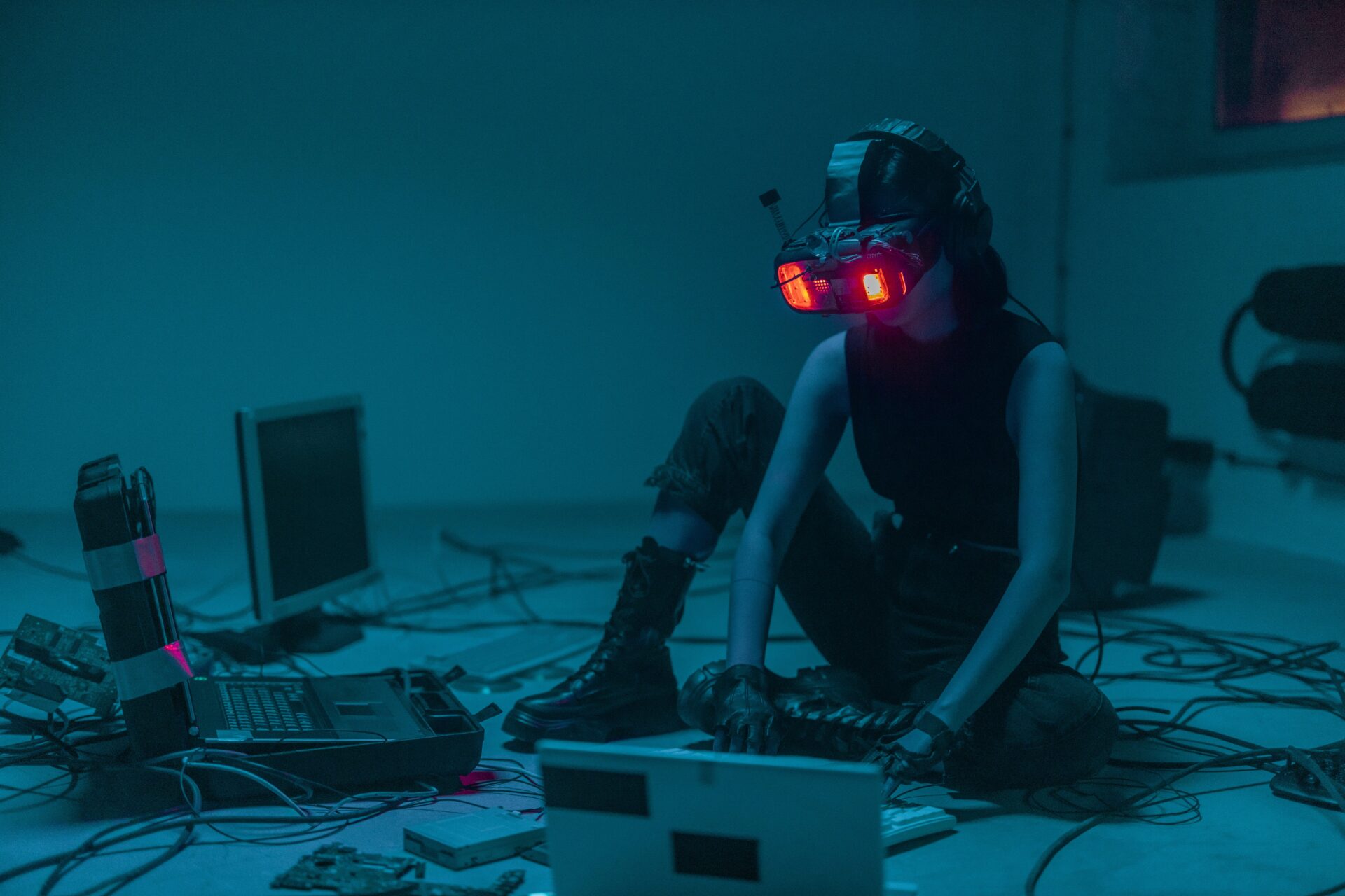 Osoba w okularach VR, siedzi na podłodze przed mrocznymi ekranami komputerów