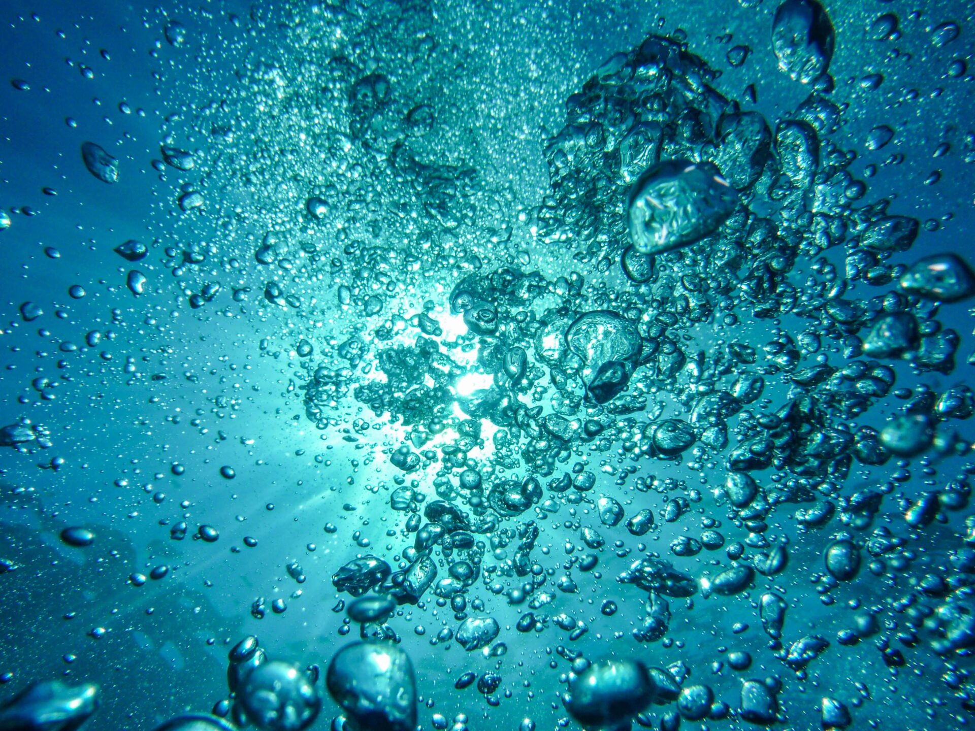Widok podwodny, bąble powietrza, prześwitujące światło przez błękitną wodę.
