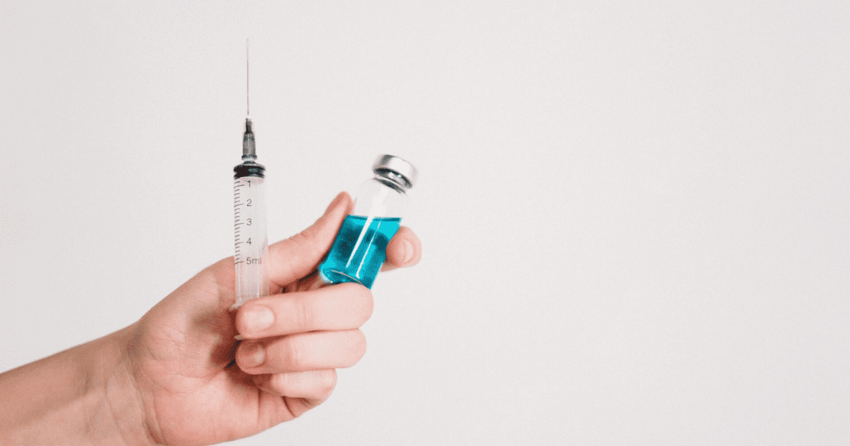 Szczepionka i fiolka z niebieskim płynem w dłoni