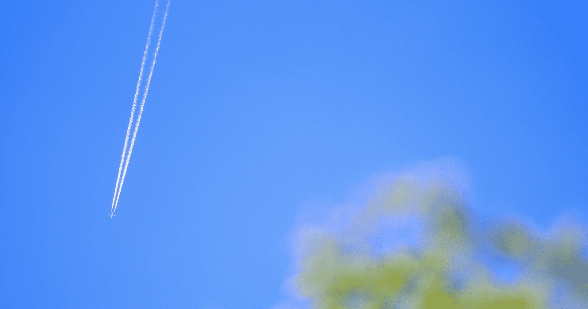 Samolot na błękitnym niebie pozostawiający za sobą smugi chemiczne