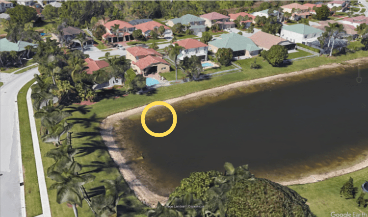 Zrzut ekranu z Google Earth – widok na staw w Moon Bay Circle z lotu ptaka. Na obrazie widać jeden ze stawów i domy rodzinne wzdłuż brzegu. W centrum obrazu znajduje się wyróżniony obszar, w którym leżał samochód z ciałem.