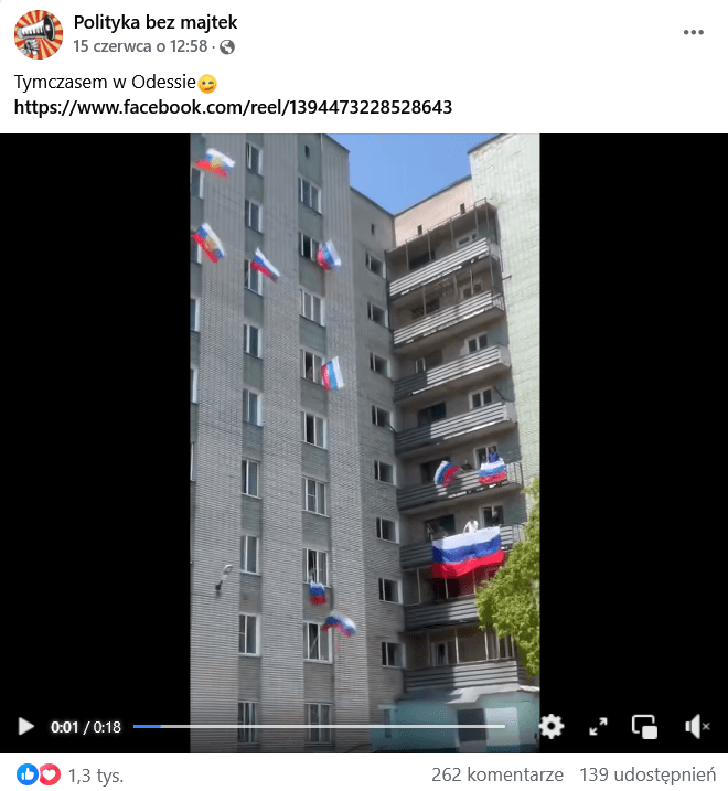 Zrzut ekranu wpisu na Facebooku. Na górze podpis i elementy interfejsu platformy, na dole klatka z nagrania przedstawiająca budynek. Z jego okien i balkonów wywieszone są rosyjskie flagi.