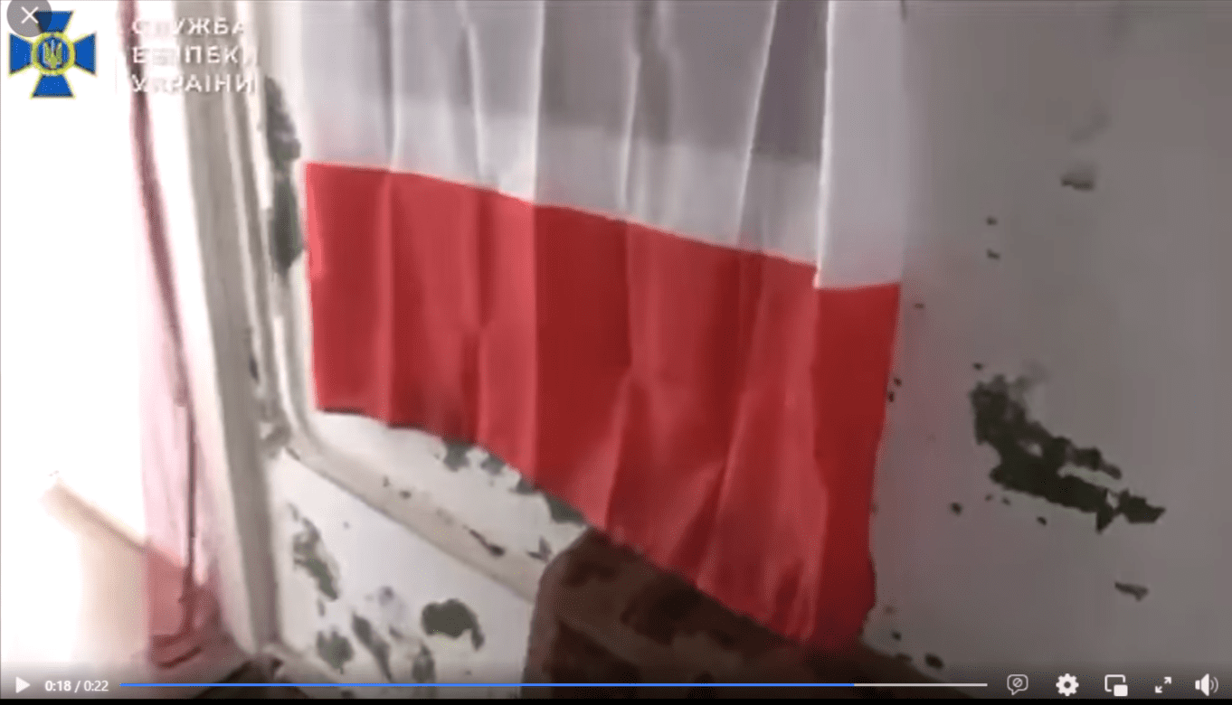Zrzut ekranu z nagrania, w którym przedstawiono zatrzymanie grupy mężczyzn. Na stopklatce widać niedbale powieszoną polską flagę na oknie przy zadrapanej ścianie.